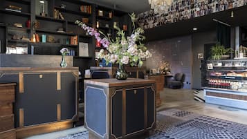 A reception desk with a vase of flowers, a bookshelf with books and decorative items, a wall of photographs, and a display case with snacks.