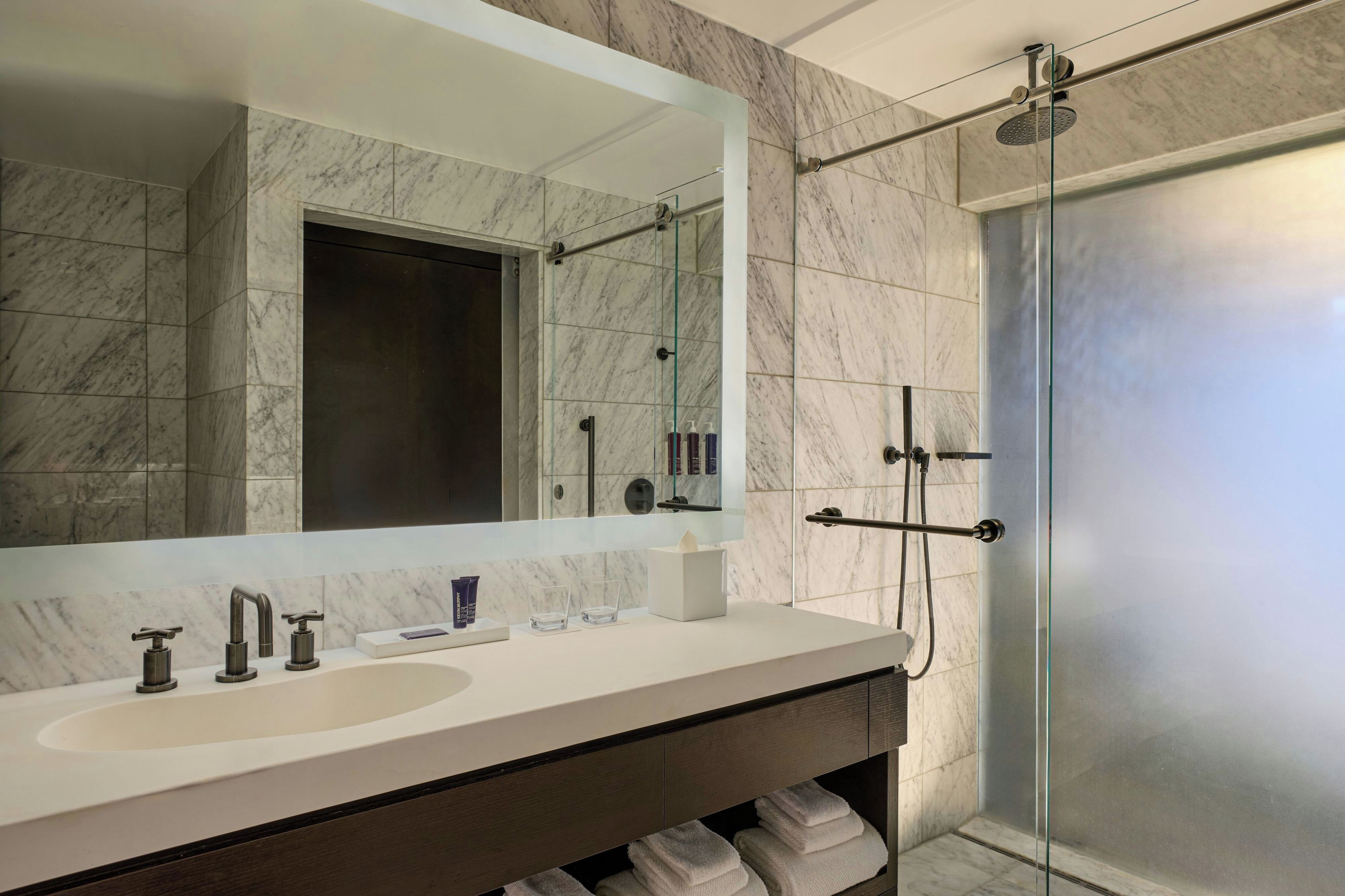 A modern bathroom with a large mirror, a sink, and a shower area.