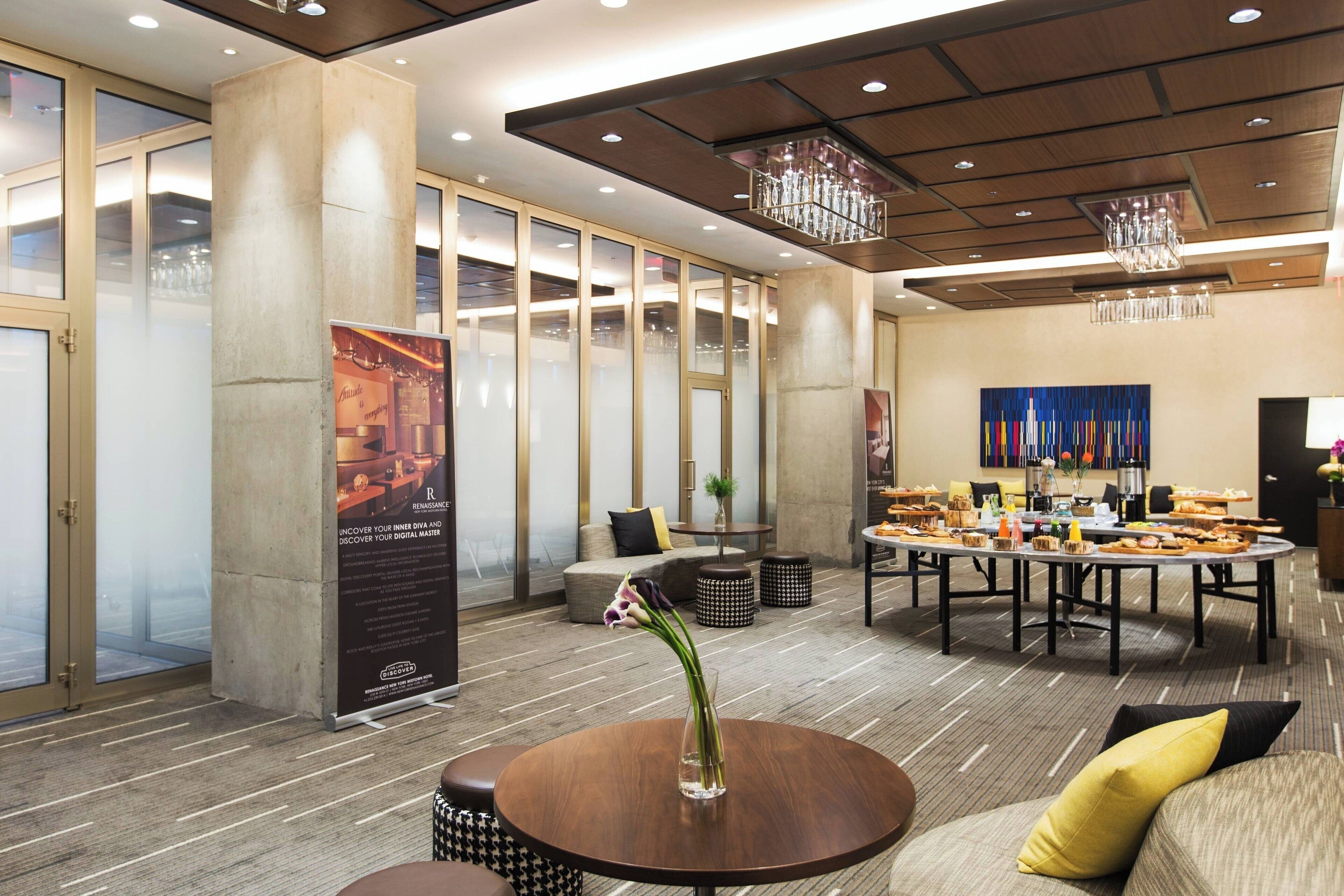 A modern hotel lobby with a round dining table, comfortable seating, and a large poster.