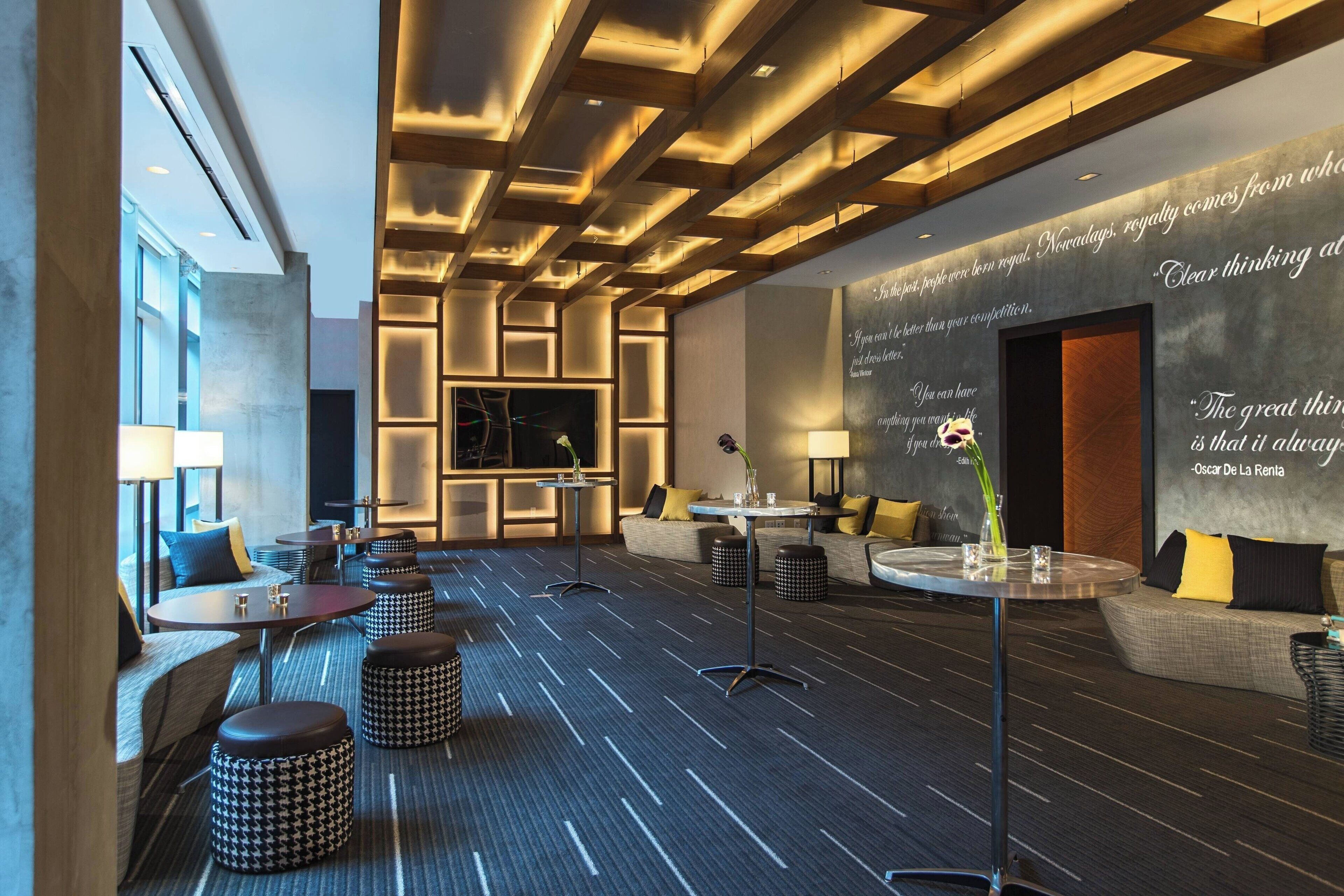Un moderno vestíbulo de hotel con una zona de estar central, una pared grande con citas inspiradoras y una variedad de opciones de asientos, incluyendo sofás y mesas redondas.