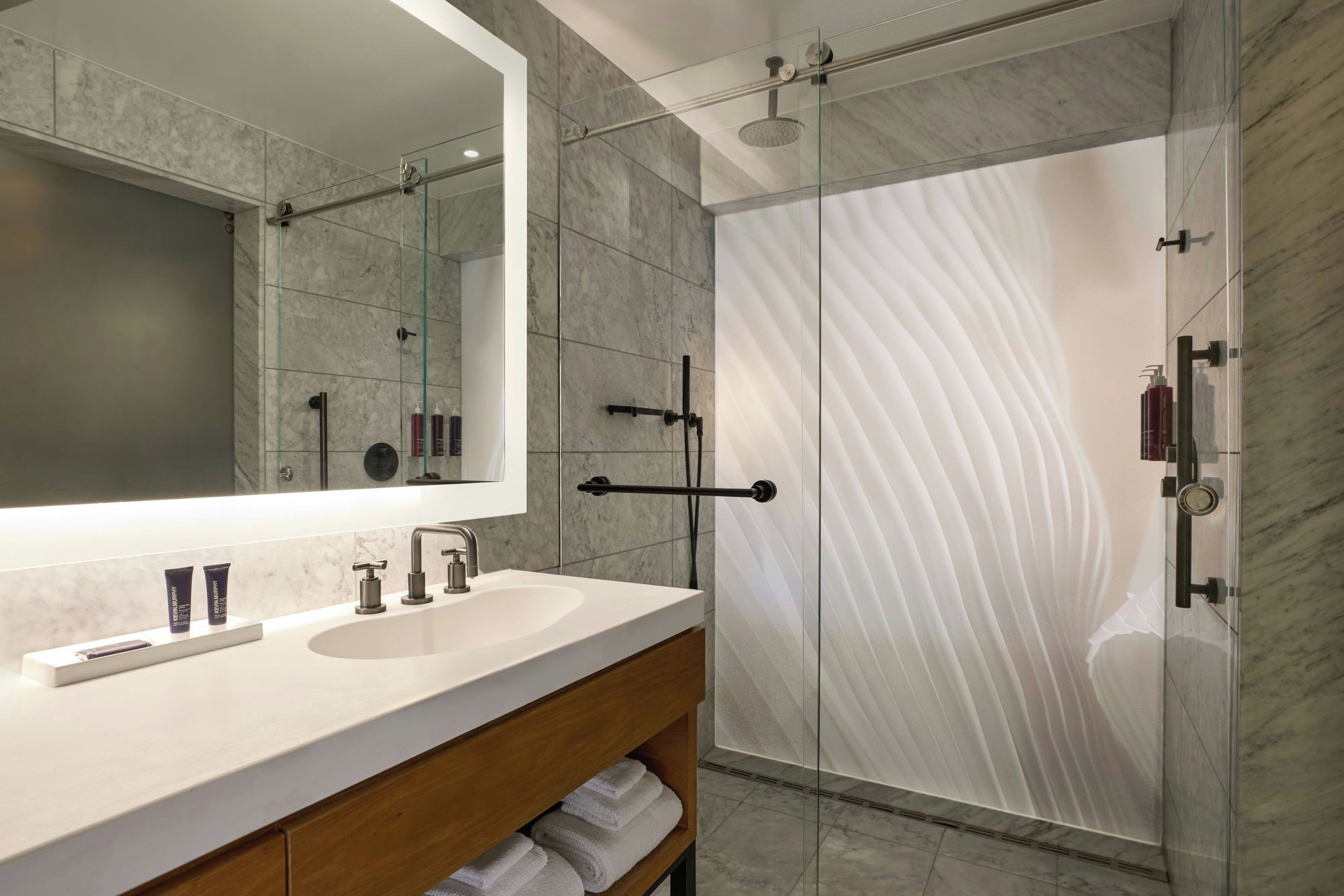 Un baño moderno con un espejo grande, lavamanos dobles y cabina de ducha con paredes de vidrio.