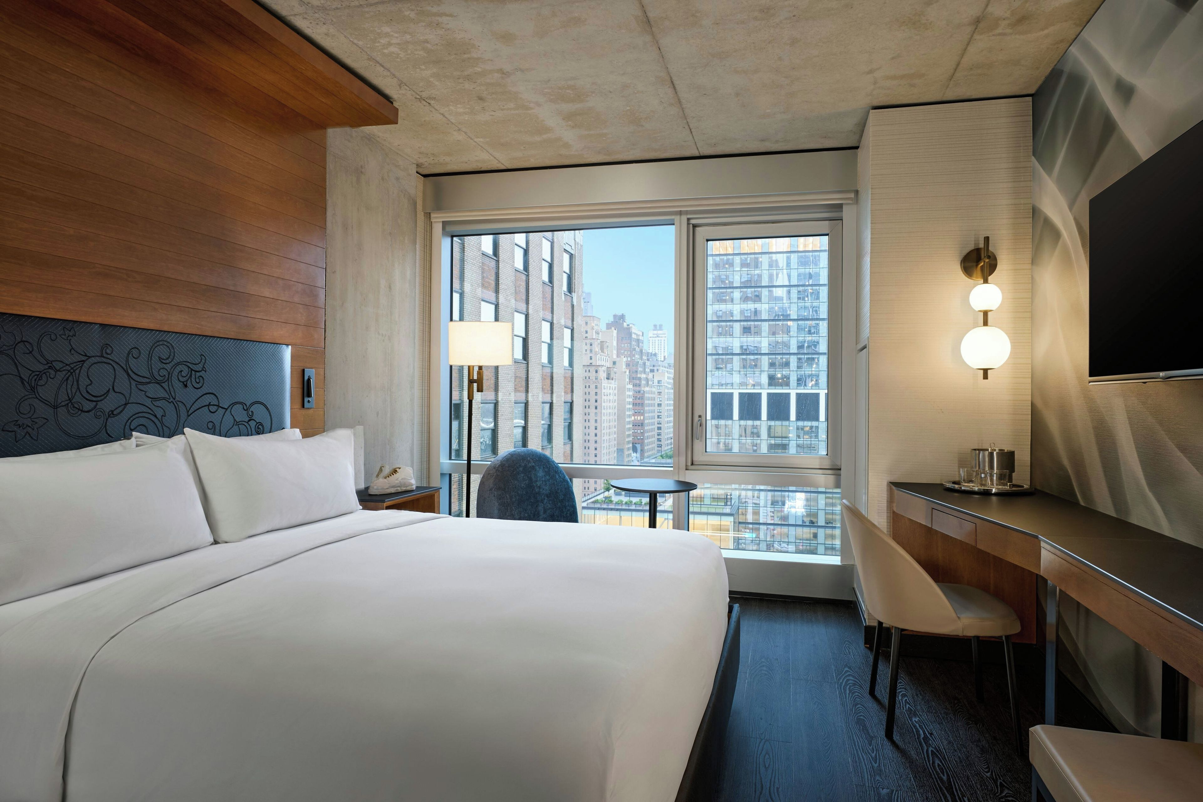 Una camera d'albergo con un letto grande, una scrivania, una sedia, un tavolino e vista sulla città dalla finestra.