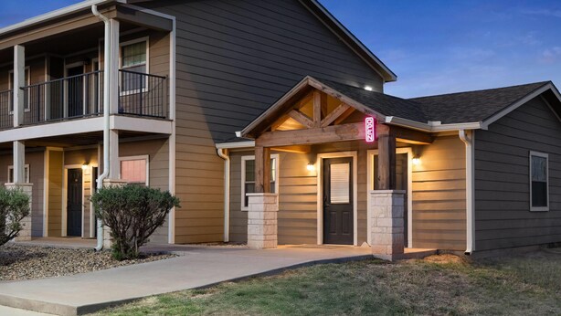 A two-story residential building with a balcony, a front porch, and a driveway. - Eagle's Den Suites Big Spring a Travelodge by Wyndham (Big Spring)