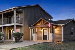 A two-story residential building with a balcony, a front porch, and a driveway. - Eagle's Den Suites Big Spring a Travelodge by Wyndham (Big Spring)