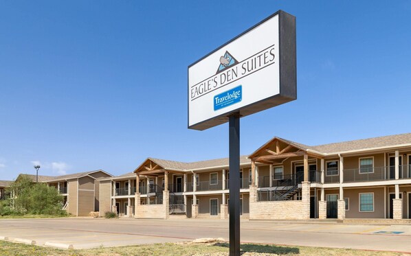 A Travelodge by Wyndham sign in front of a building with multiple balconies and a stone facade. - Eagle's Den Suites Big Spring a Travelodge by Wyndham (Big Spring)