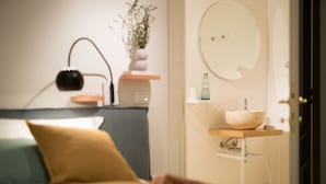 A bedroom with a bed, bedside table, lamp, and a bathroom with a sink and mirror. - B&B Santa Maria del Fiore (Florence)