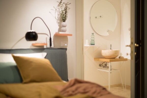 A bedroom with a bed, bedside table, lamp, and a bathroom with a sink and mirror. - B&B Santa Maria del Fiore (Florence)