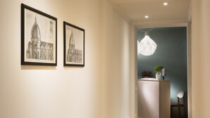 A hallway with two framed architectural drawings on the wall, a pendant light, a small table with a plant, and a chair. - B&B Santa Maria del Fiore (Florence)