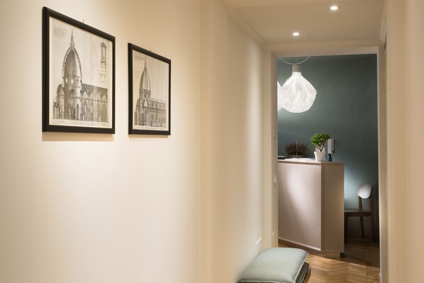 A hallway with two framed architectural drawings on the wall, a pendant light, a small table with a plant, and a chair. - B&B Santa Maria del Fiore (Florence)