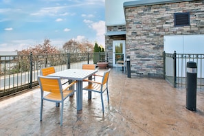 Un patio exterior con una mesa, sillas, un muro de piedra y vistas a la calle.