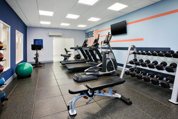 Un gimnasio con cintas de correr, elípticas, una prensa de banca y una barra de mancuernas.