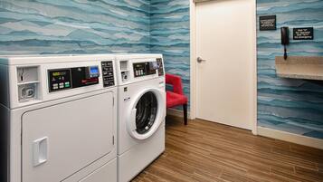 A laundry area with a front-loading washer and dryer, a red chair, and a door with emergency contact instructions.
