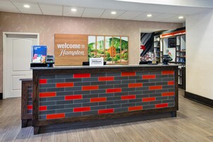 Una recepción con un letrero que dice 'Welcome to Hampton', una placa de 'Hilton Honors' y vistas del área de recepción.