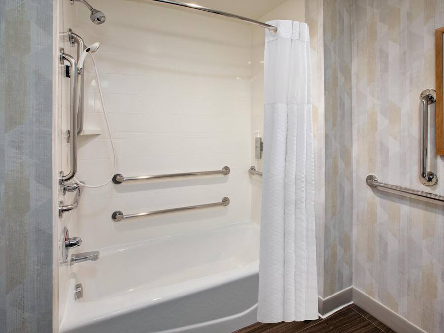 A modern bathroom with a walk-in shower, grab bars, and a framed picture on the wall.