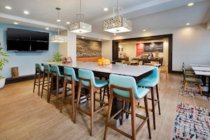 Cocina moderna con una isla central, taburetes de bar y un comedor con televisor montado en la pared.