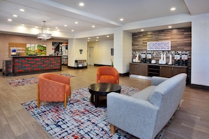 Vestíbulo de hotel con mostrador de recepción, zona de estar y estación de café.