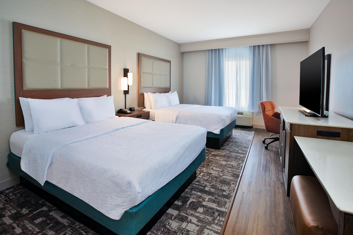Una habitación de hotel con dos camas, un escritorio, un televisor y una silla.