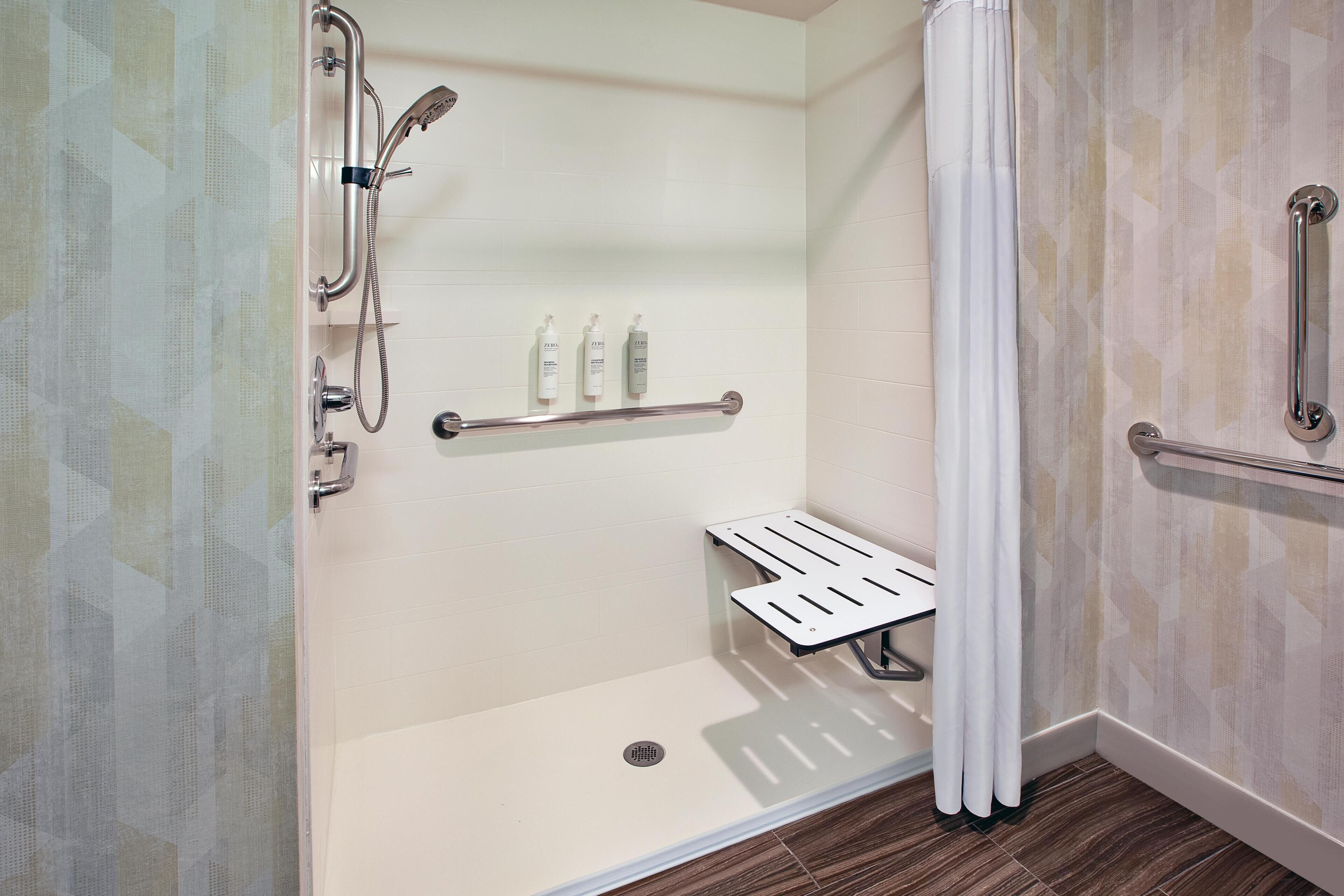 A modern bathroom with a walk-in shower, grab bars, and a shelf with toiletries.