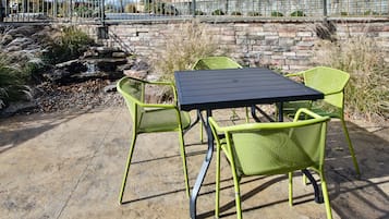 Un patio al aire libre con una mesa y sillas, un muro de piedra y una pequeña cascada.