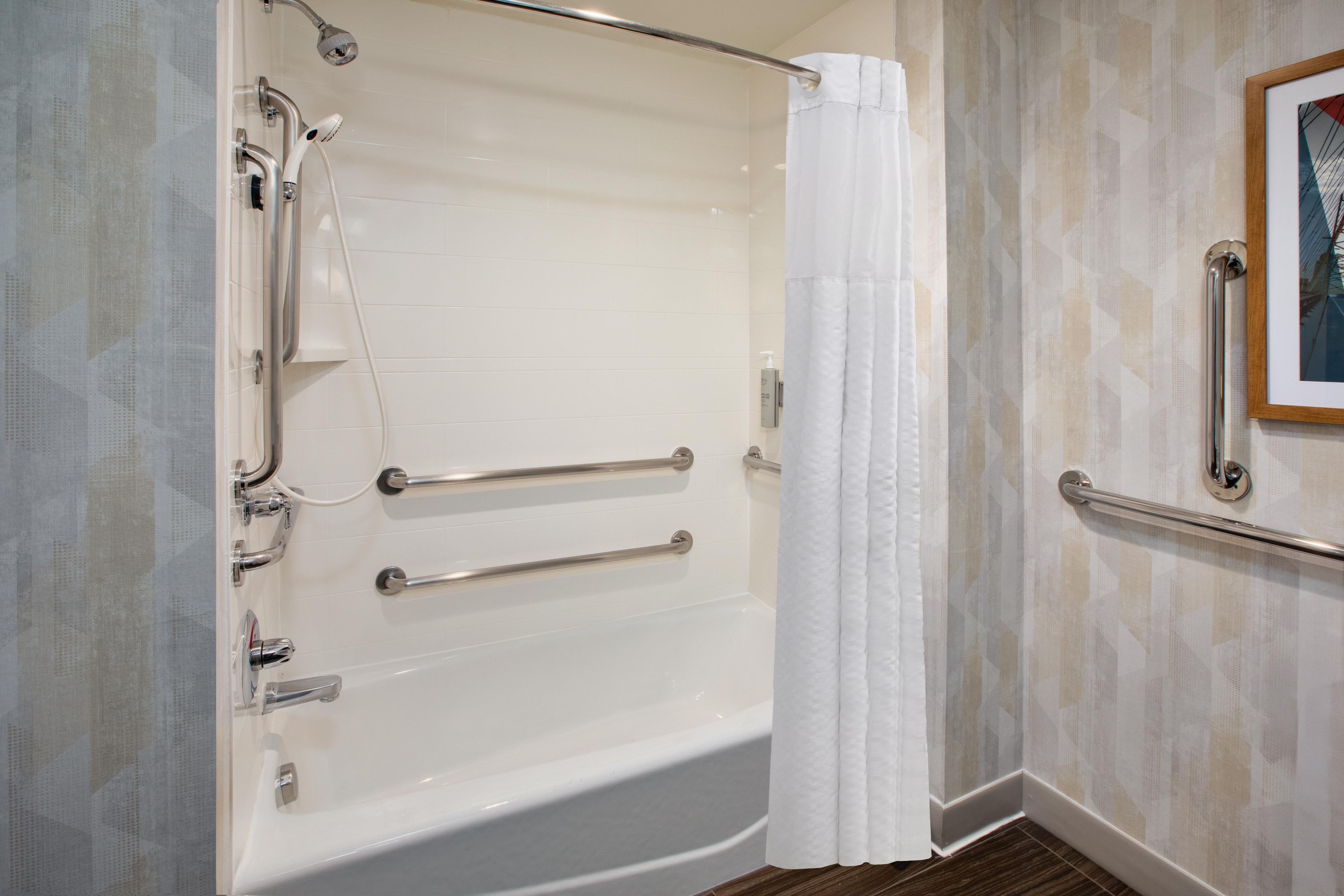 A white bathtub with a shower head, grab bars, and a curtain.