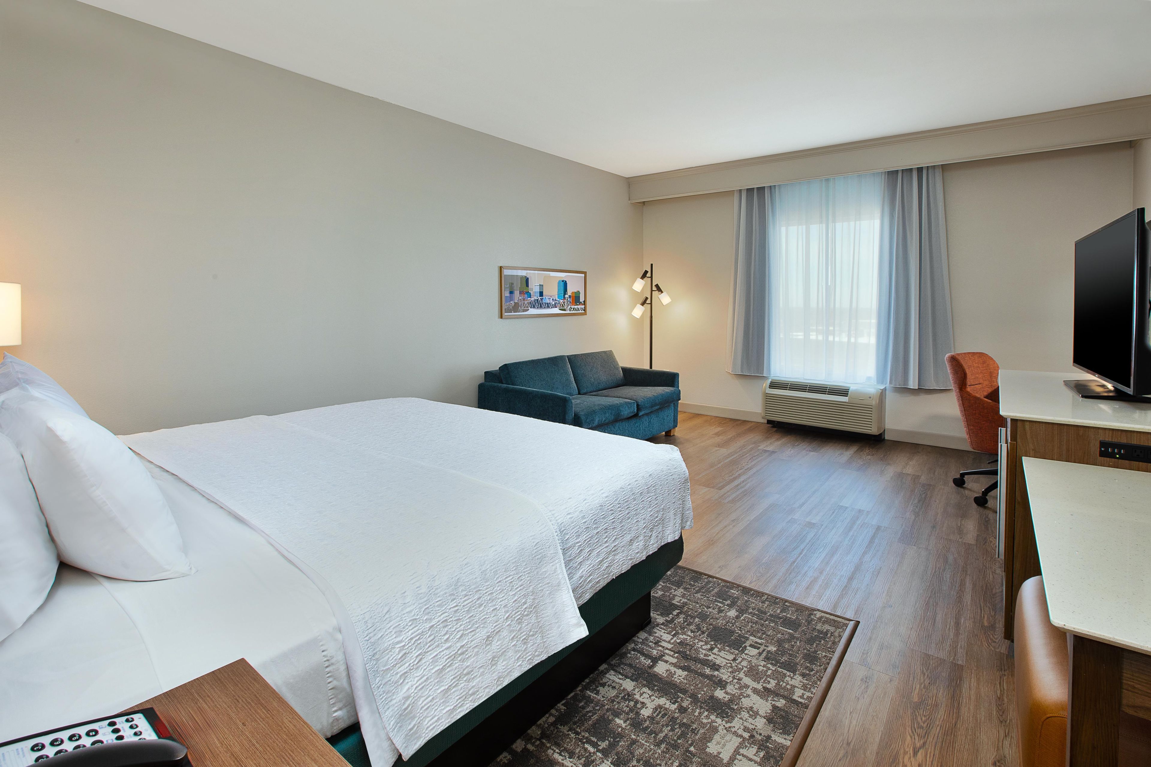 A hotel room with a bed, a desk, a chair, a television, and a window with curtains.