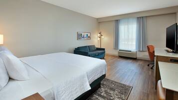 A hotel room with a bed, a desk, a chair, a television, and a window with curtains.