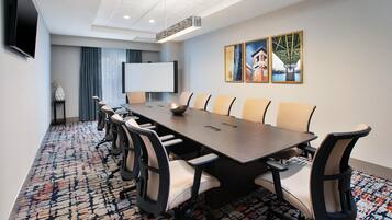 Uma sala de conferências com uma mesa comprida, cadeiras, um projetor e um quadro branco.