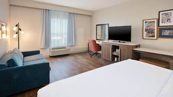 A hotel room with a bed, a desk, a chair, a TV, and a window with curtains.