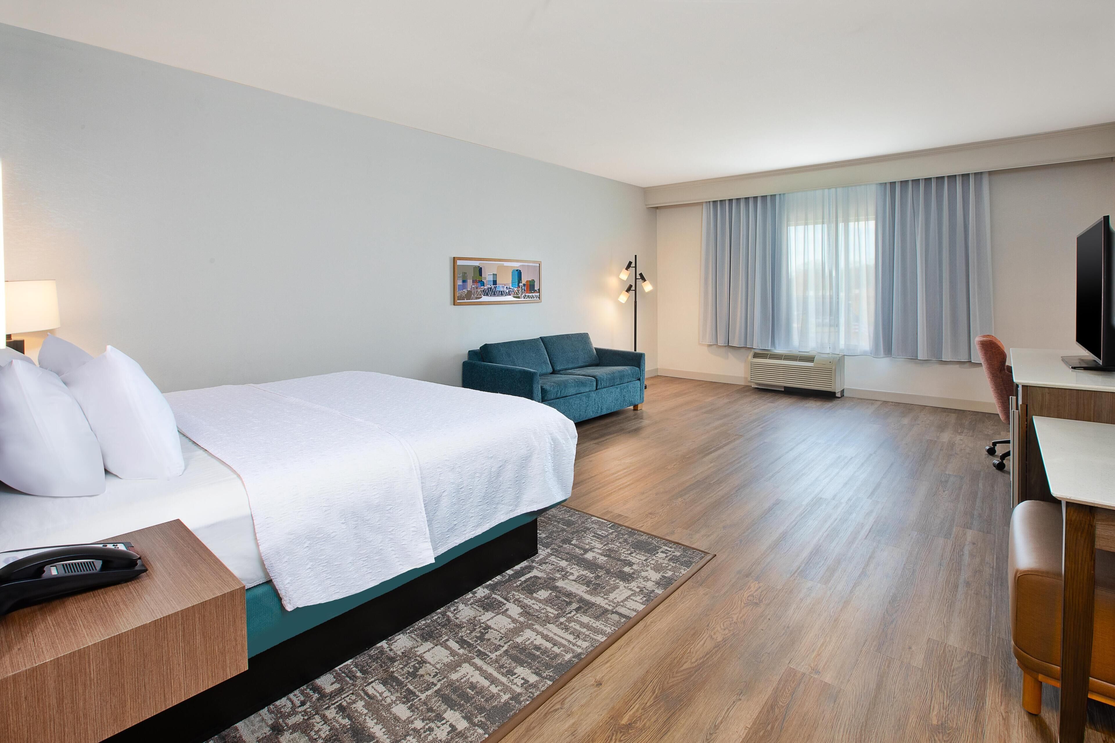 A hotel room with a bed, a desk, a chair, a TV, and a window with curtains.