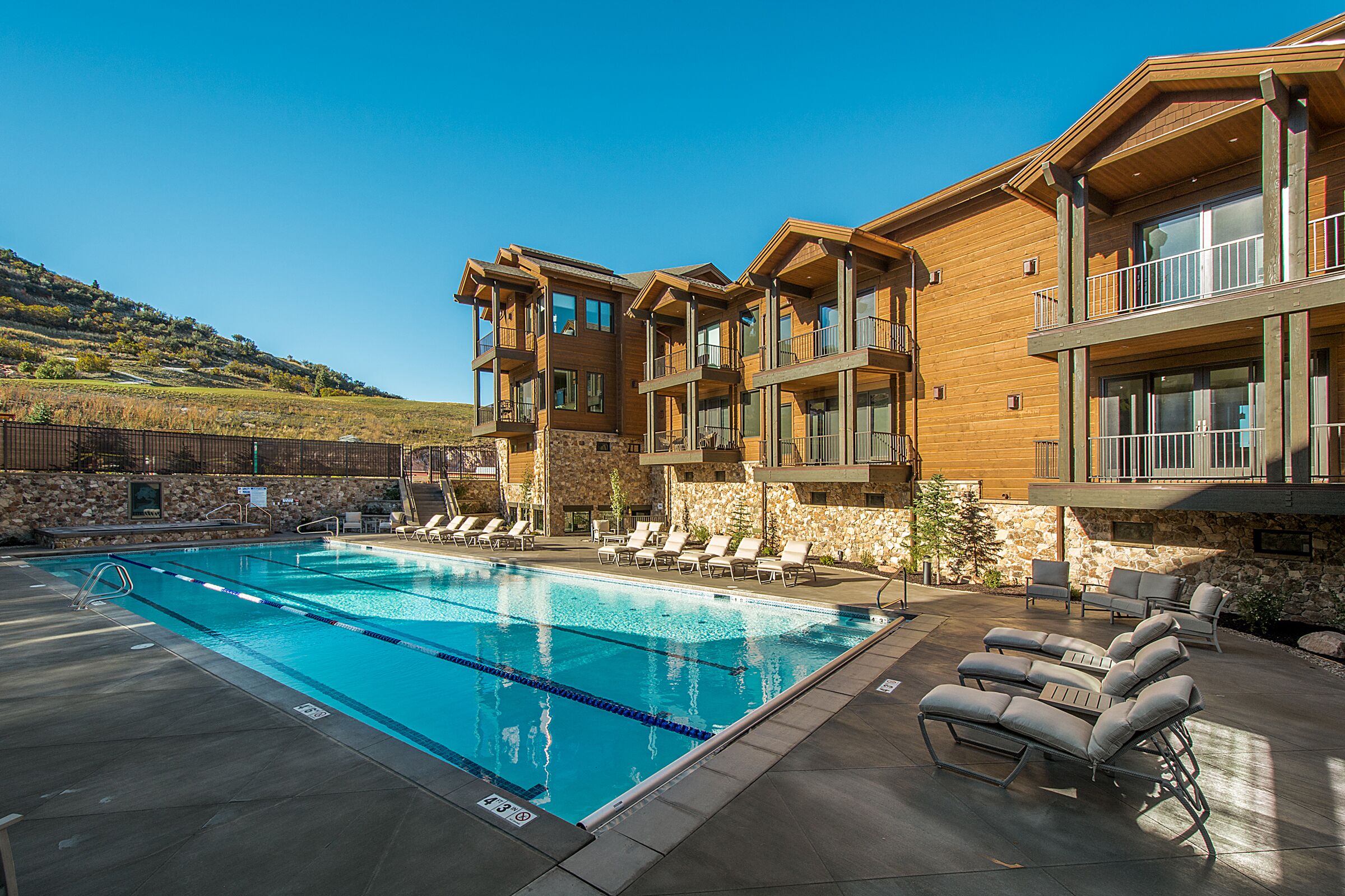 A modern hotel with a swimming pool, outdoor seating, and a stone facade.