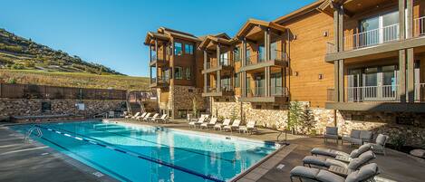 A modern hotel with a swimming pool, outdoor seating, and a stone facade.