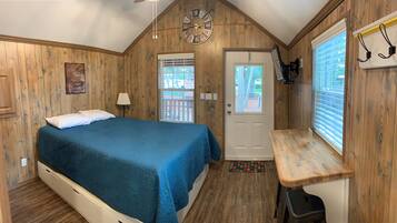 Un dormitorio con una cama, una puerta, una ventana, un reloj de pared y una mesita.