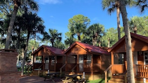 Una hilera de cabañas de madera con porches anexos, mesas de picnic y una zona de patio de ladrillo.