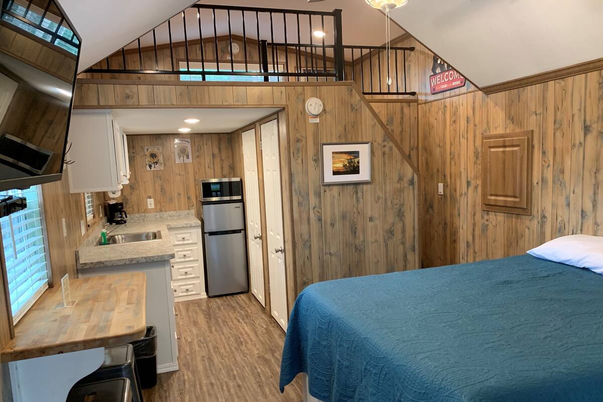 A compact room with a kitchenette, a bed, and a staircase leading to an upper level.