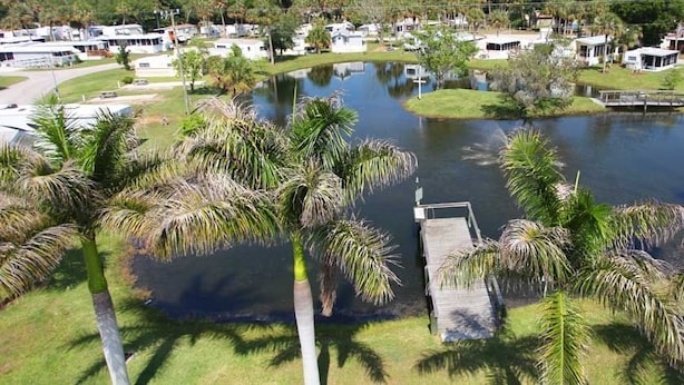 Una propiedad frente al lago con muelle, palmeras y vehículos recreativos.