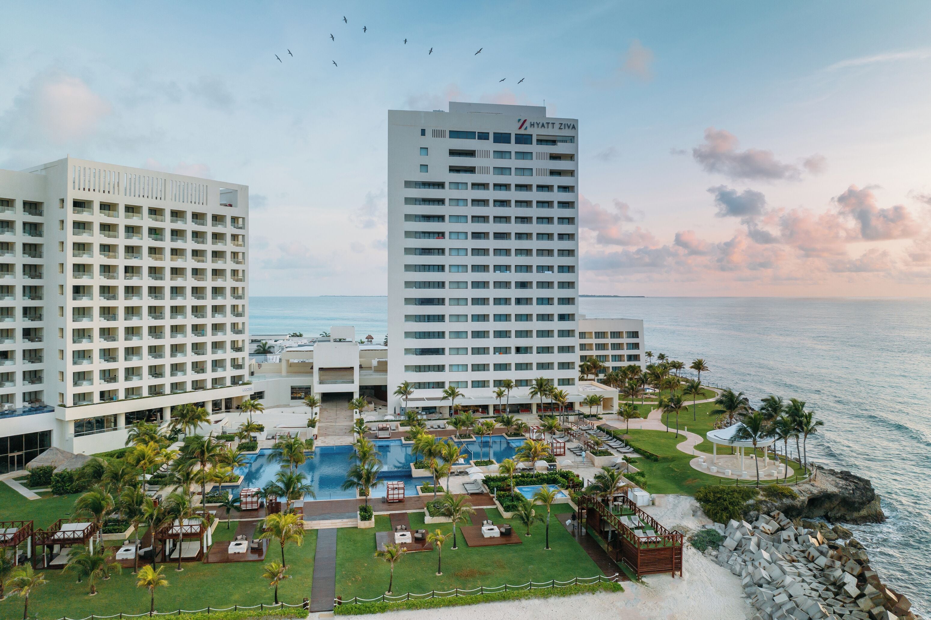 A resort with multiple buildings, a large pool area, and a view of the ocean.