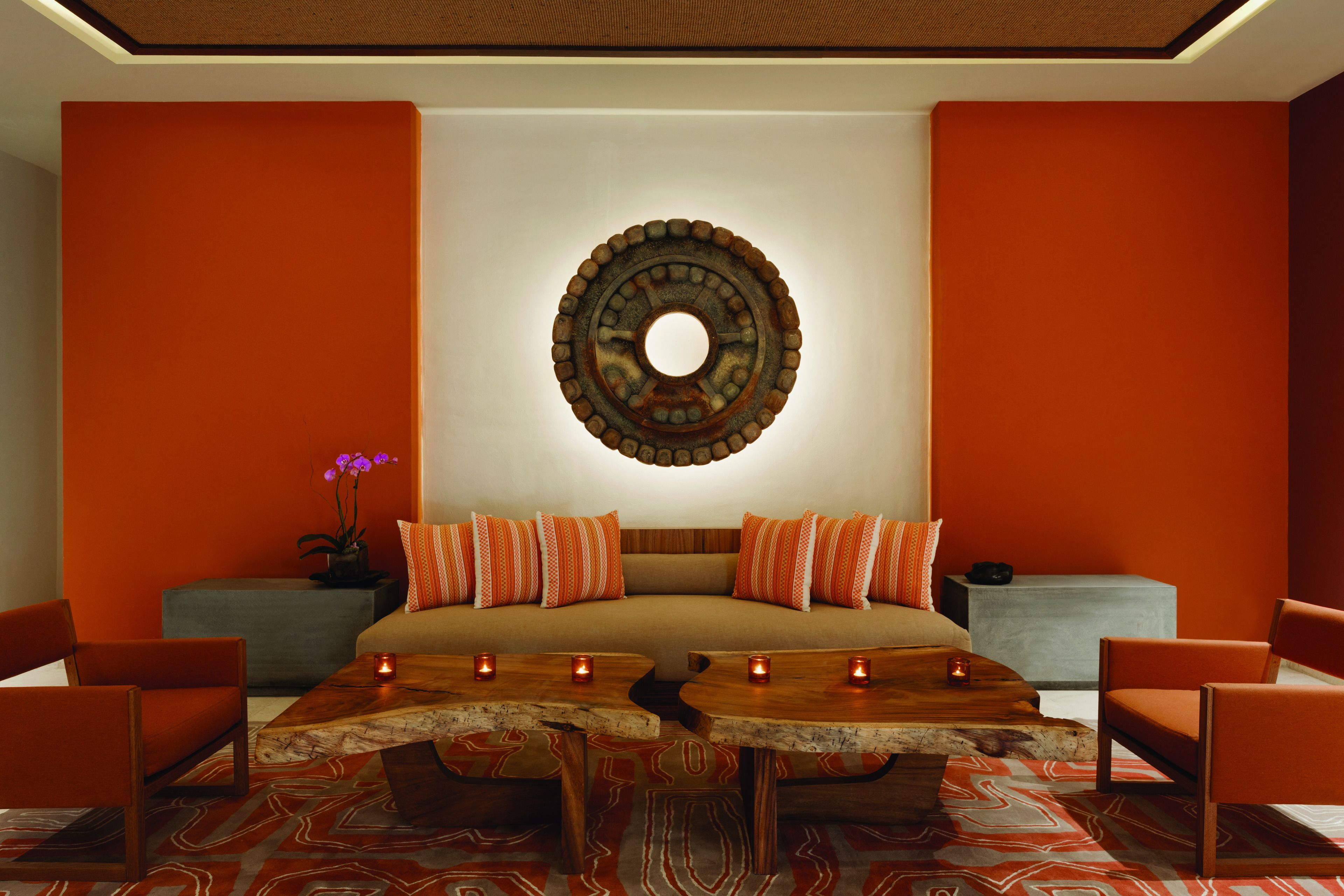 Una habitación moderna con una cama grande, paredes anaranjadas, un adorno circular en la pared y una mesa de centro de madera con velas.