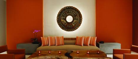 Una habitación moderna con una cama grande, paredes anaranjadas, un adorno circular en la pared y una mesa de centro de madera con velas.