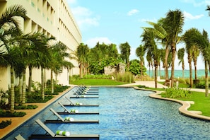 A pool area with lounge chairs and palm trees, surrounded by a building with a white facade.