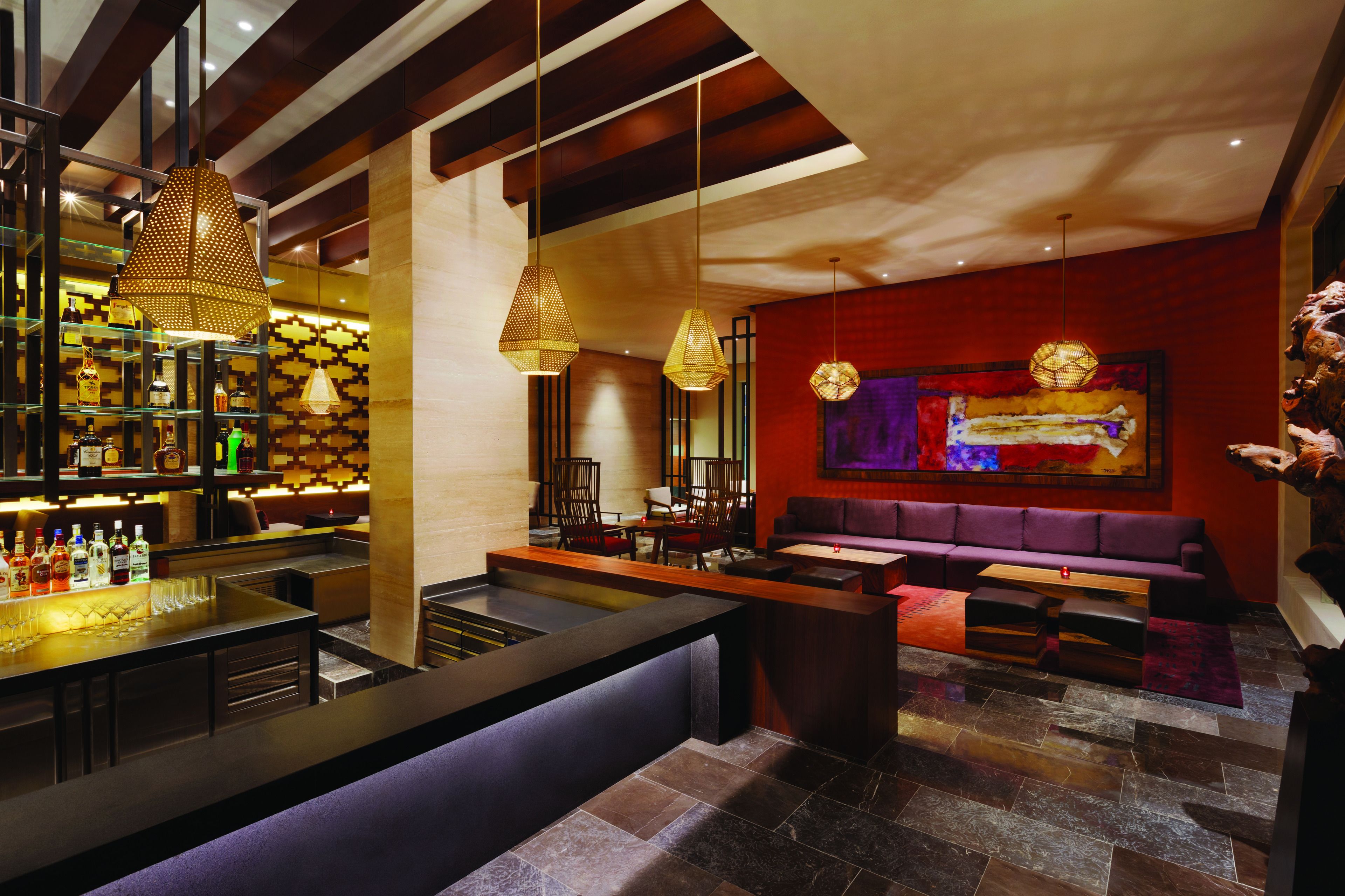 Zona de bar moderna con una barra larga, asientos e iluminación colgante.