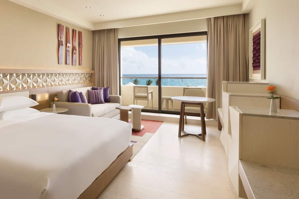 Habitació d'hotel amb un llit gran, una escriptori, una cadira, una taula petita i vista a l'oceà.