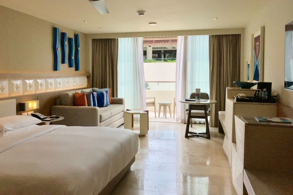 Habitació d'hotel amb un llit gran, un sofà, una taula de treball i un balcó amb cortines.
