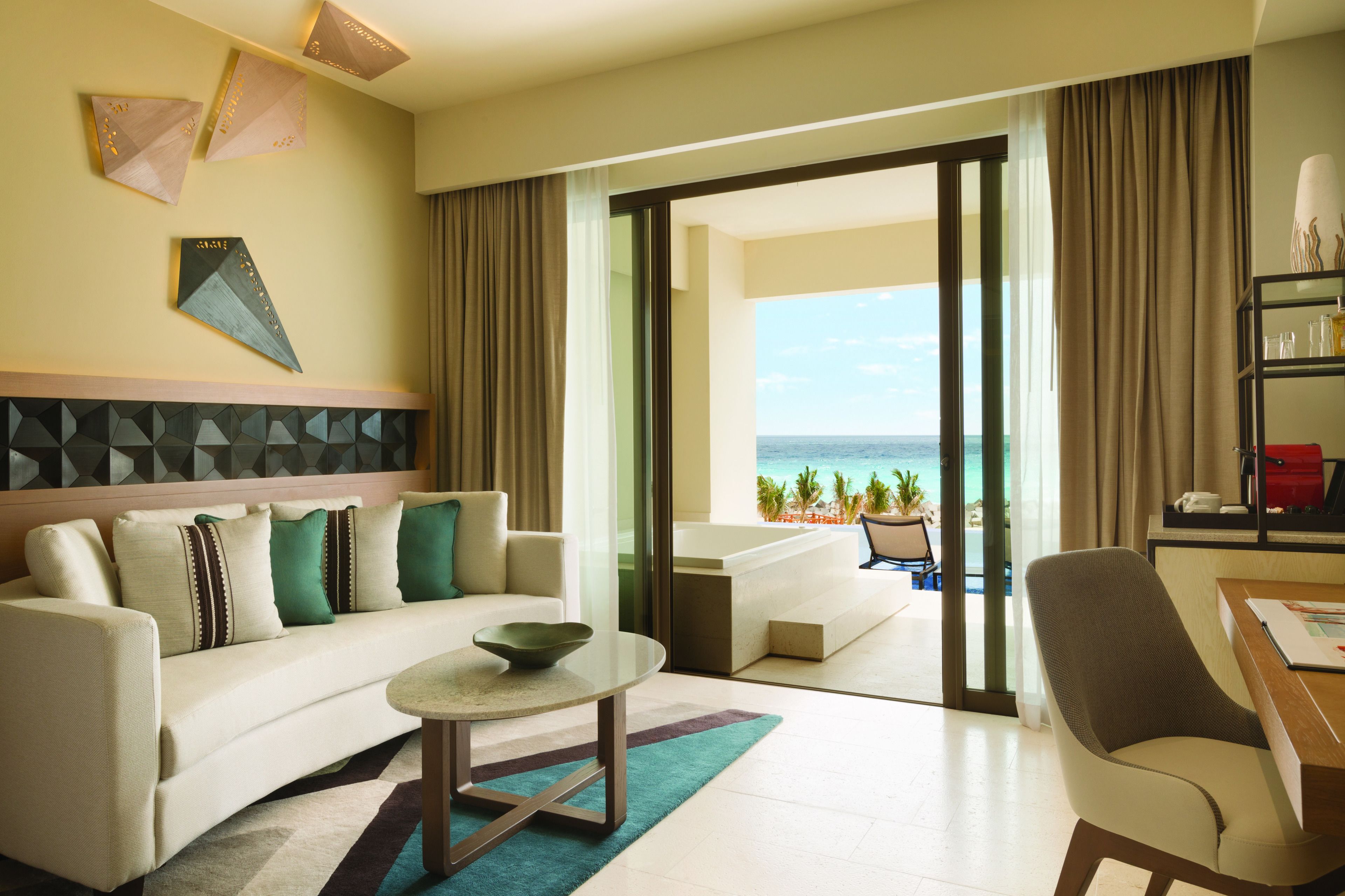 A modern hotel room with a sofa, a coffee table, a desk, and a view of the ocean.