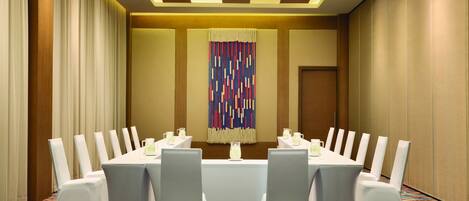 A conference room with a long table, white chairs, and a colorful abstract wall decoration.