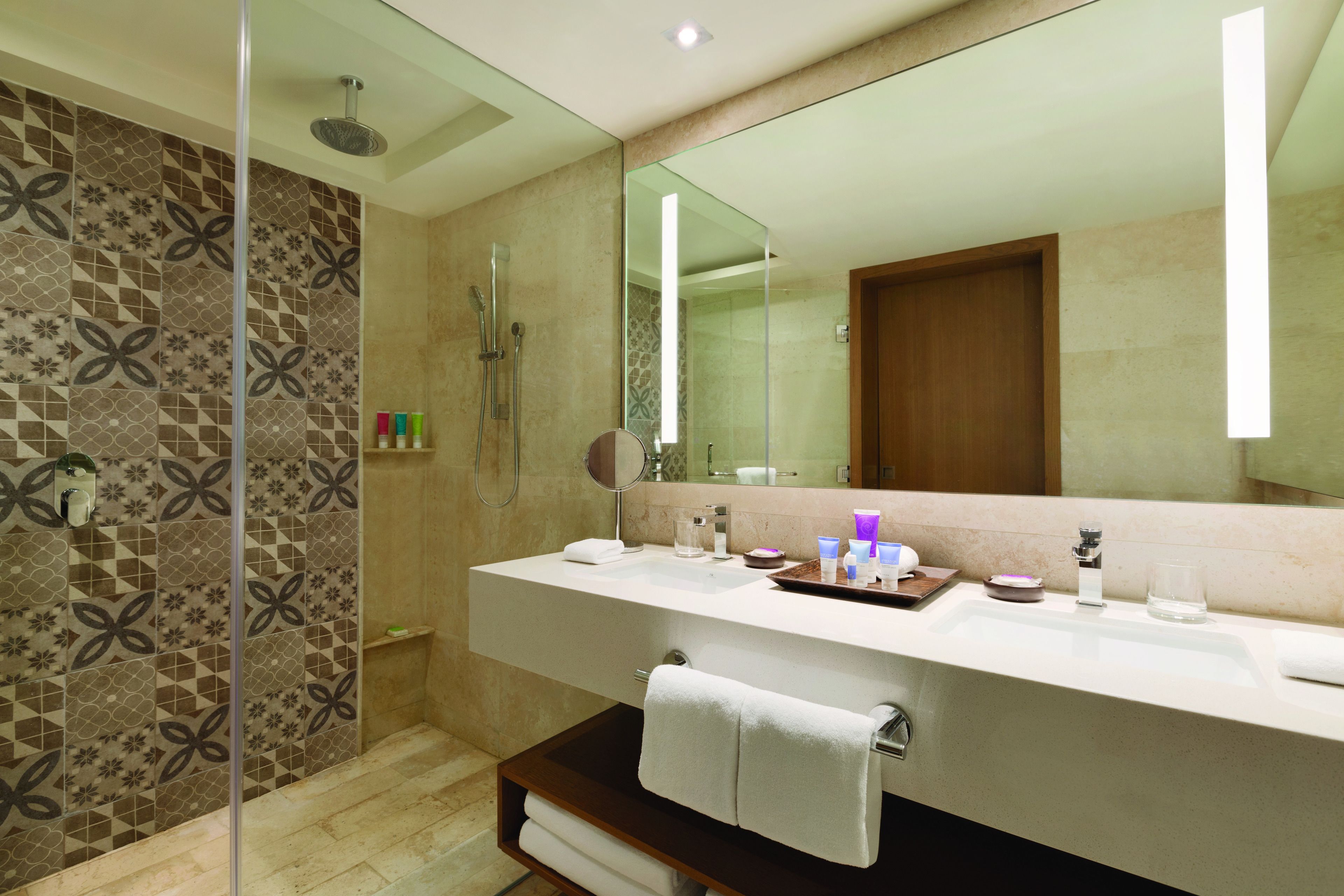 A modern bathroom with a large mirror, two sinks, and a shower area.