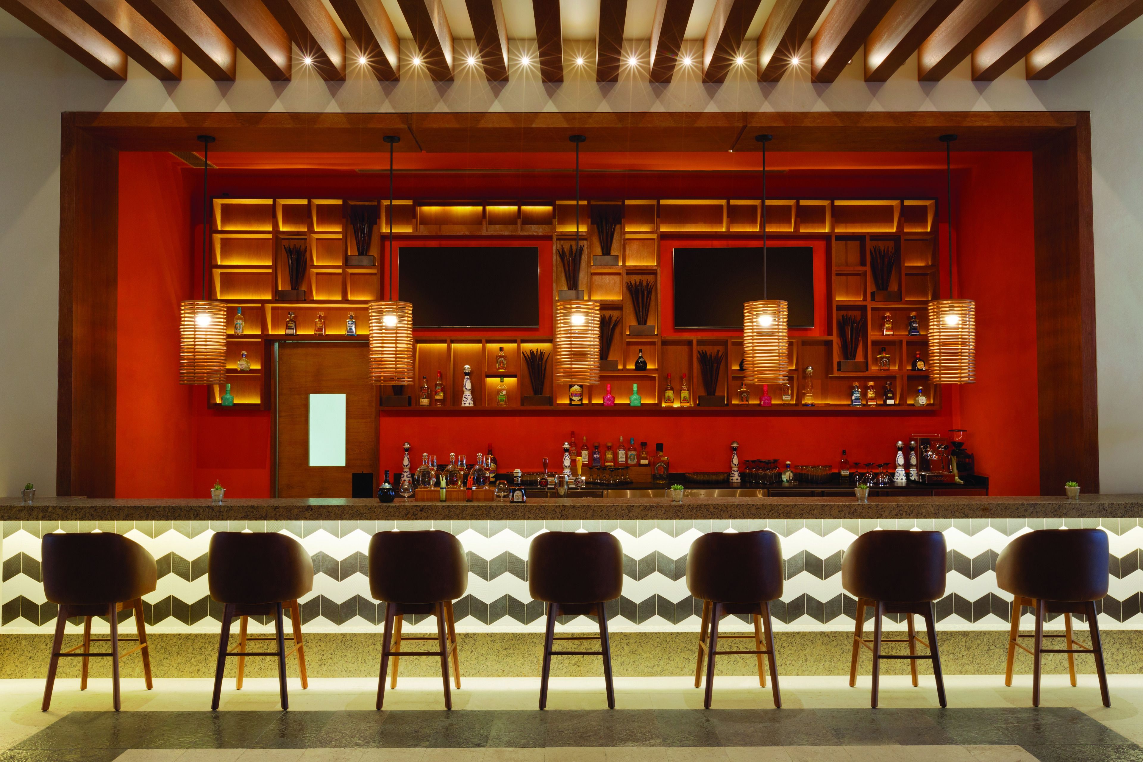 A bar area with a red accent wall, multiple shelves with bottles, and three bar stools.