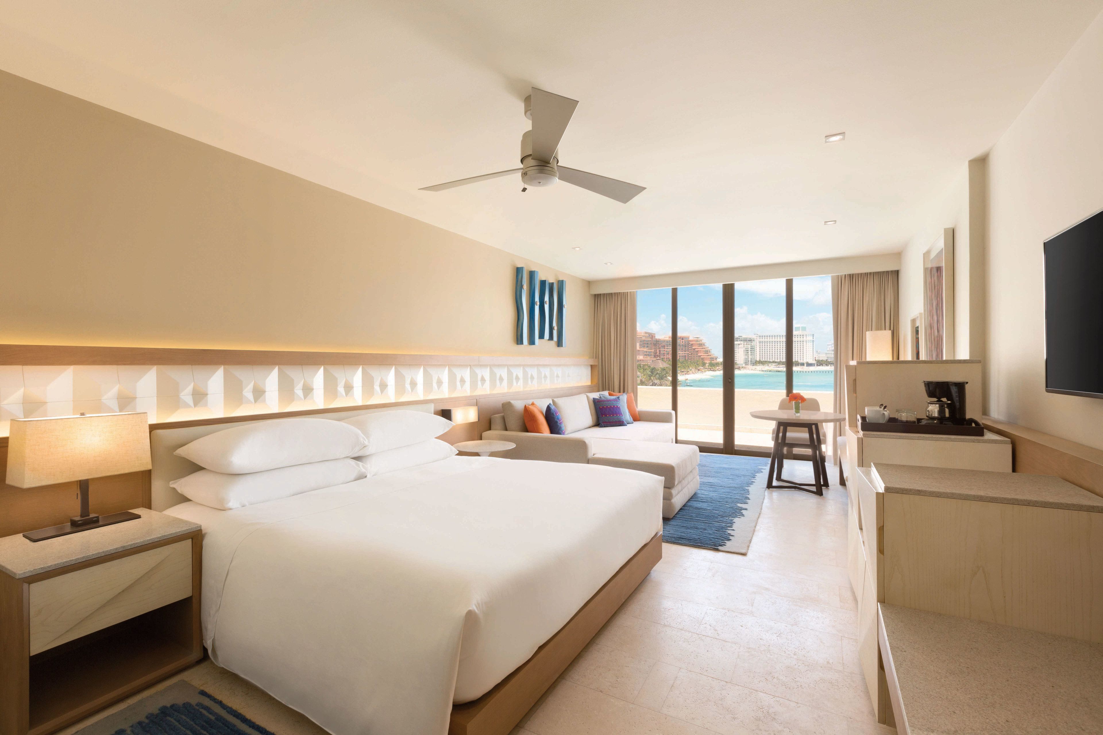 Habitación de hotel con una cama grande, un escritorio, una silla y un televisor. Se aprecia una ventana con vistas a la ciudad.
