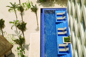 An aerial view of a swimming pool with lounge chairs, palm trees, and a thatched-roof hut.