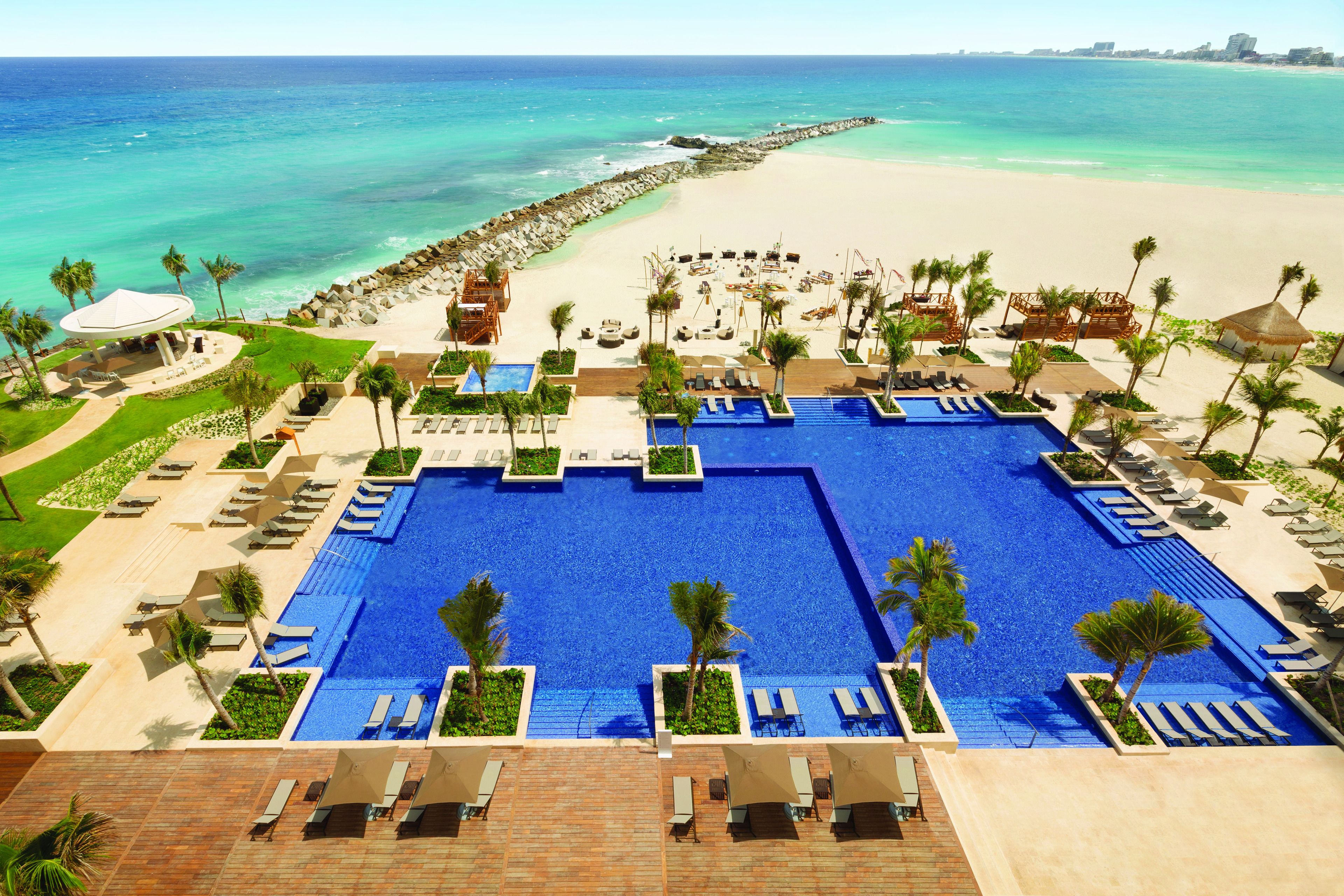 Un resort con una amplia piscina central, varias zonas de descanso y vistas a la playa.