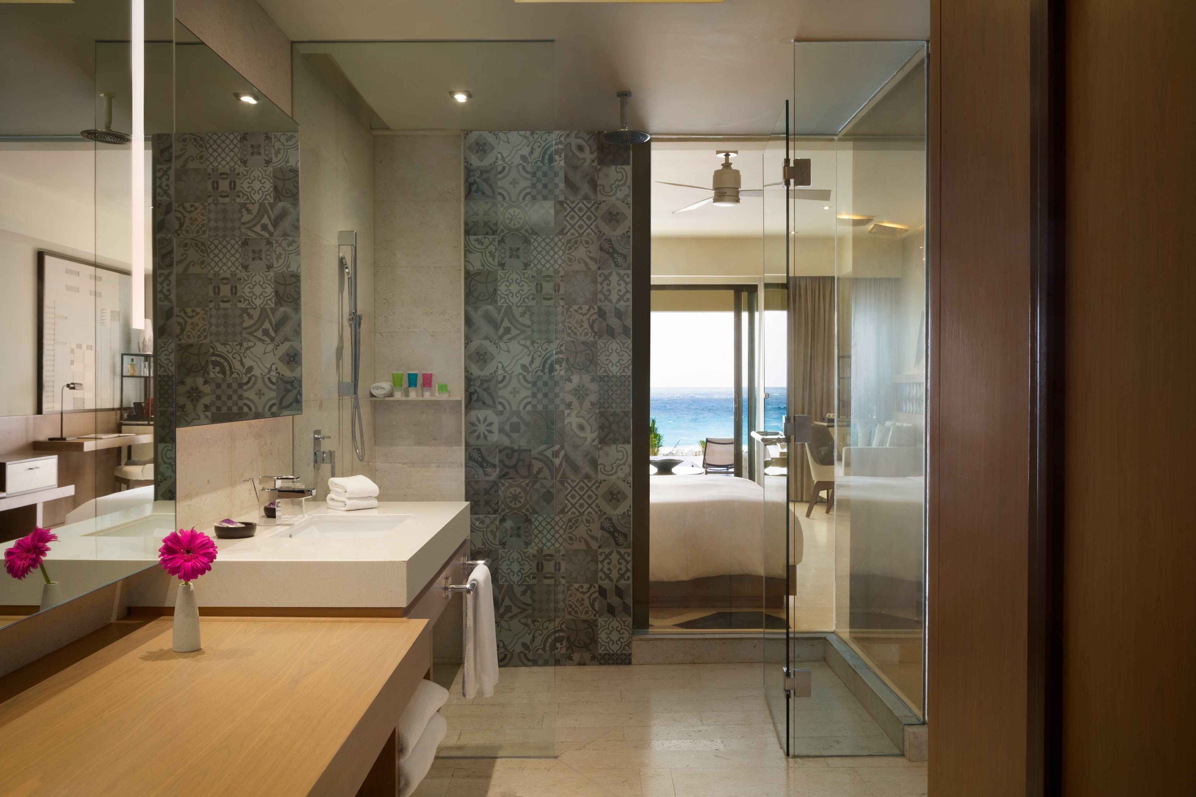 A modern bathroom with a large mirror, a shower, and a view of the beach.